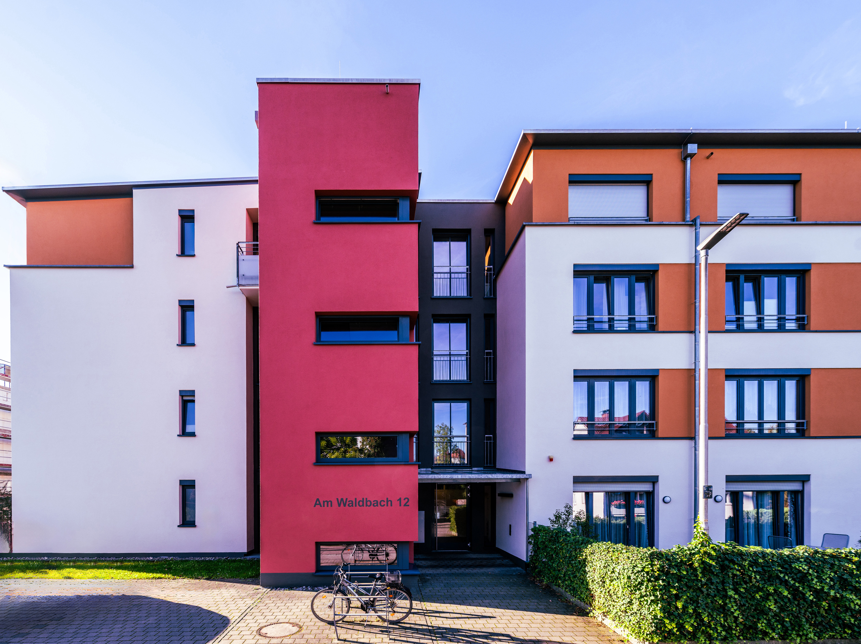Links und rechts vierstöckige Baukörper, um 90° gegeneinander gedreht. Dazwischen Treppenturm mit Fensterbändern. Die Nische zwischen Treppenturm und rechtem Teil ist schwarz und beherbegt den Eingang.